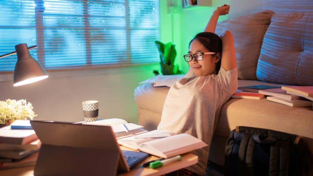 A woman is sitting at a desk; she is at home at night; she is relaxing.