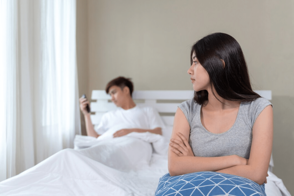 Sad woman sitting on edge of bed with pensive husband