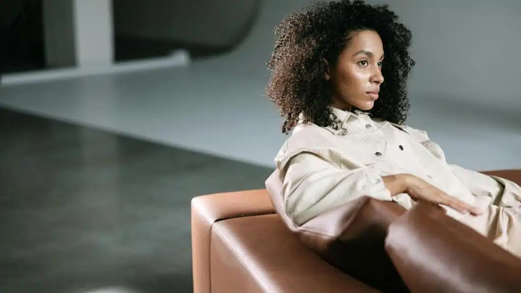A woman with curly hair sitting in a chair indoors and looking off to the side.