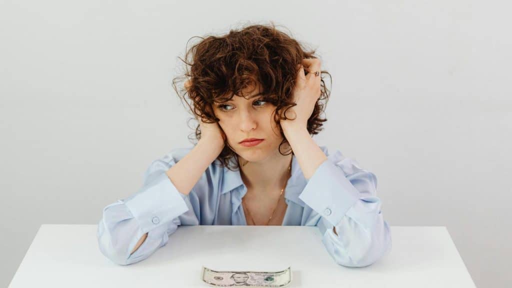 A woman looking worried at a dollar bill on a table.