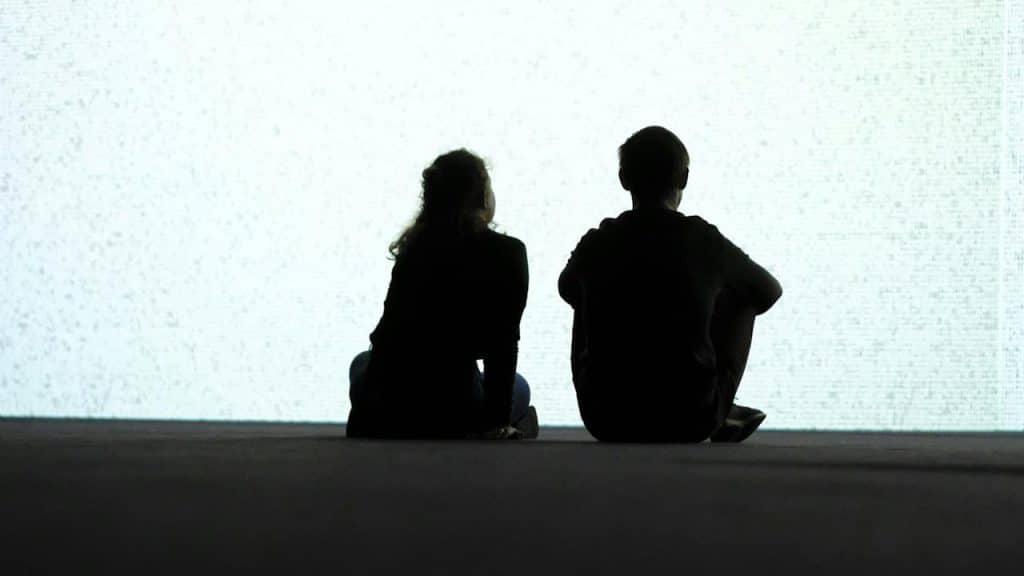 A couple sit and gaze at the bright background.