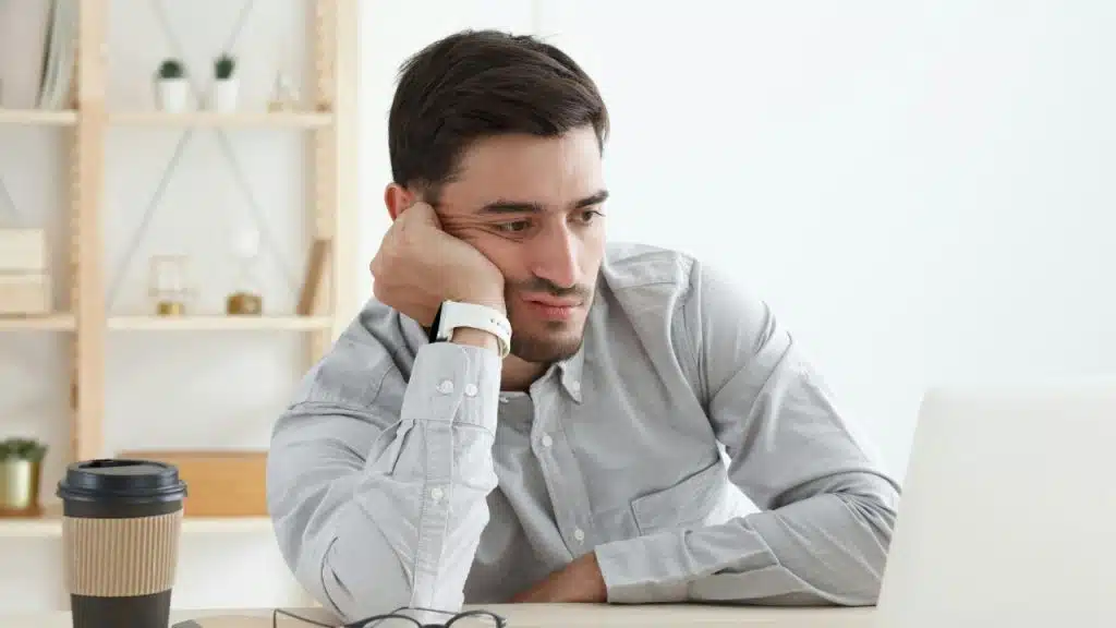 A man rests his head on his hand while looking at a laptop screen.