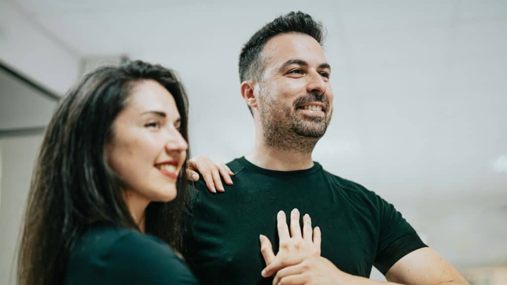 A woman rests her hand on the shoulder of a smiling man dancing.