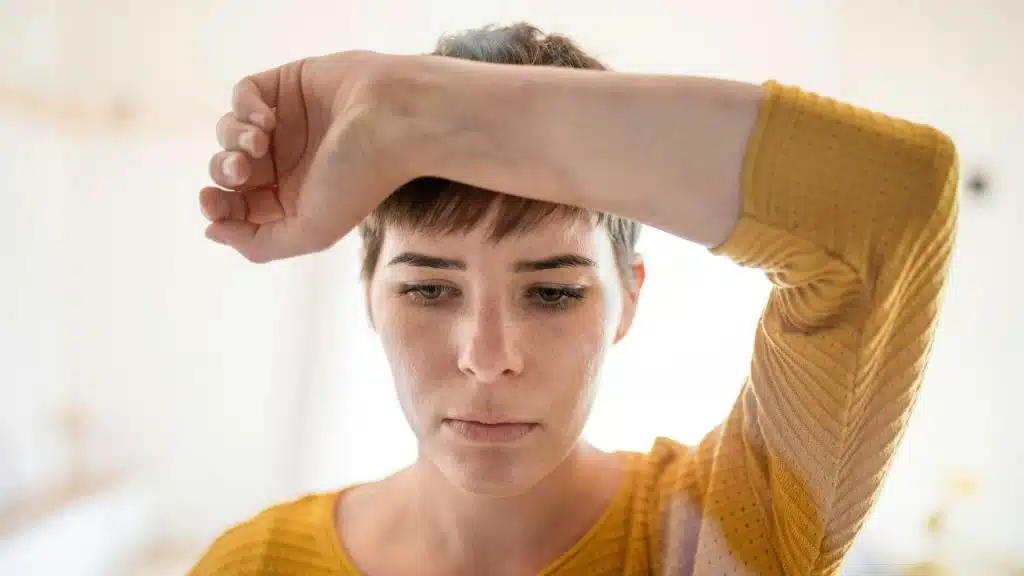 A person with short hair wearing a yellow shirt rests their forearm across their forehead.