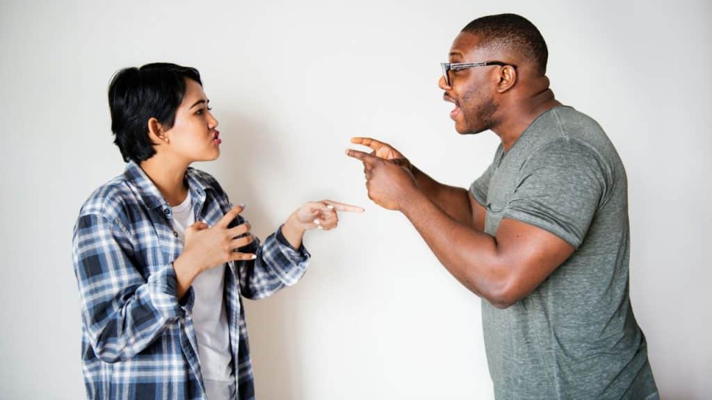 A woman and a man stand facing each other while gesturing with their hands and fingers.