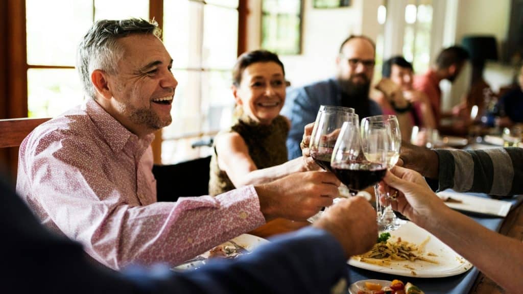 A group of people sits around a table toasting with glasses of red wine.