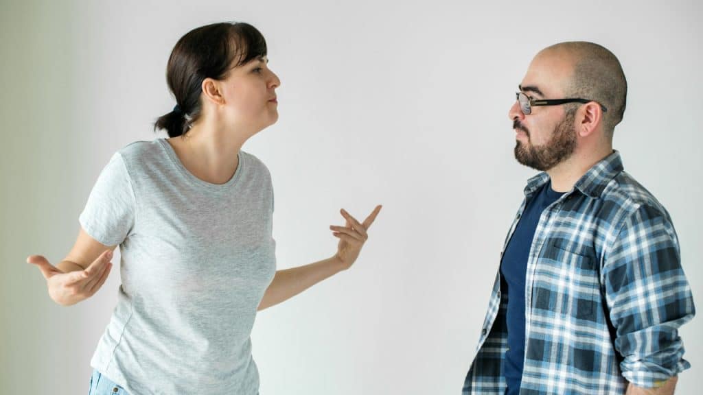 A woman in a grey shirt gestures with both hands toward a bearded man.