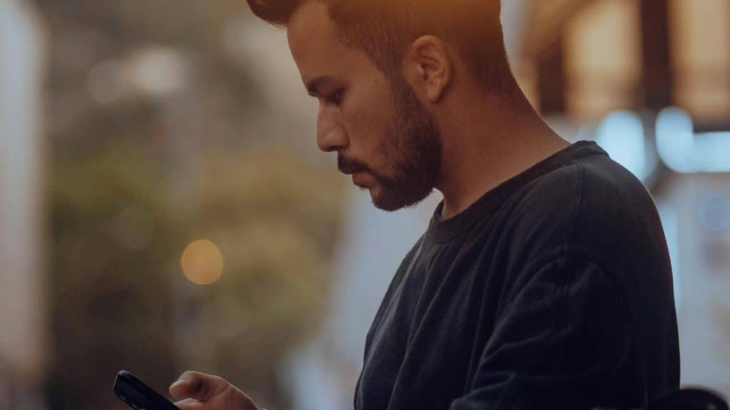 A man looking at his smartphone while standing outdoors.