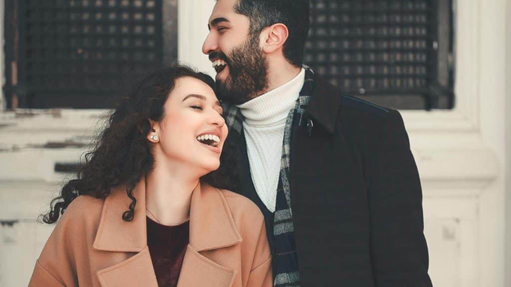 A laughing couple standing close together outdoors.
