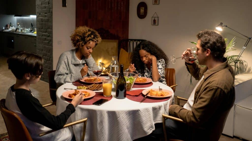 Four people sit around a circular dinner table while a man drinks from a glass.