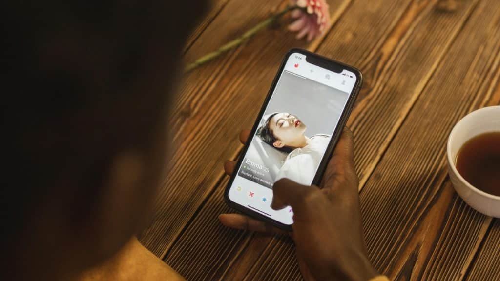 A hand holds a smartphone showing a dating profile with a photo of Emma.
