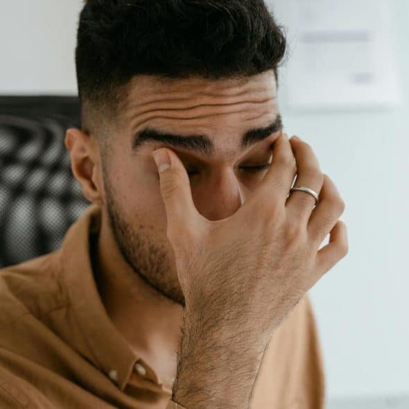 A tired man rubbing his eyes while sitting in an office chair.
