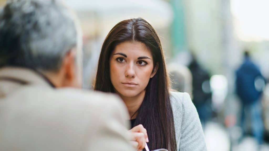 A woman with long dark hair listens intently to someone across a table.