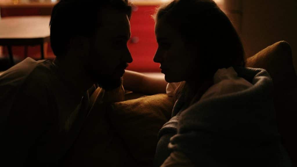A couple sitting close and facing each other in dim light.