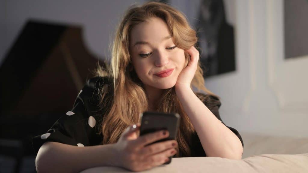 A woman smiling while looking at her smartphone indoors.