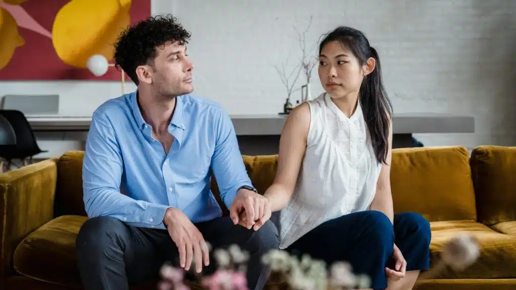 A man and a woman hold hands while sitting on a yellow sofa.