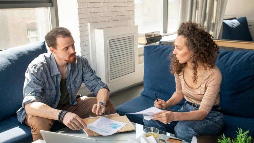 A man and woman sit on a blue couch reviewing several papers together.