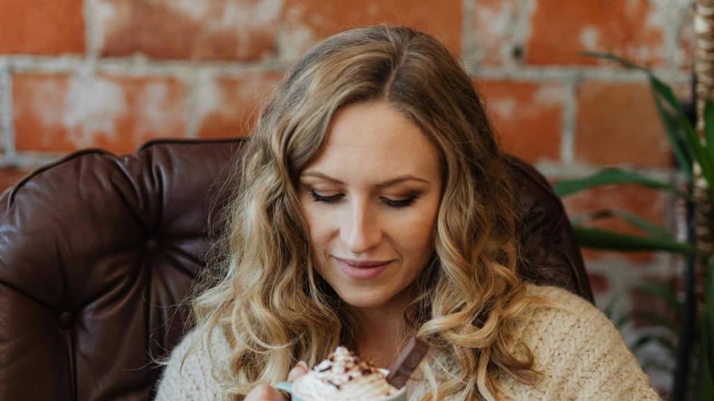 A woman in a leather chair looking down at a mug of hot chocolate with whipped cream.