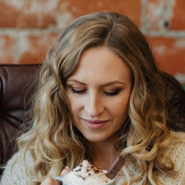 A woman in a leather chair looking down at a mug of hot chocolate with whipped cream.