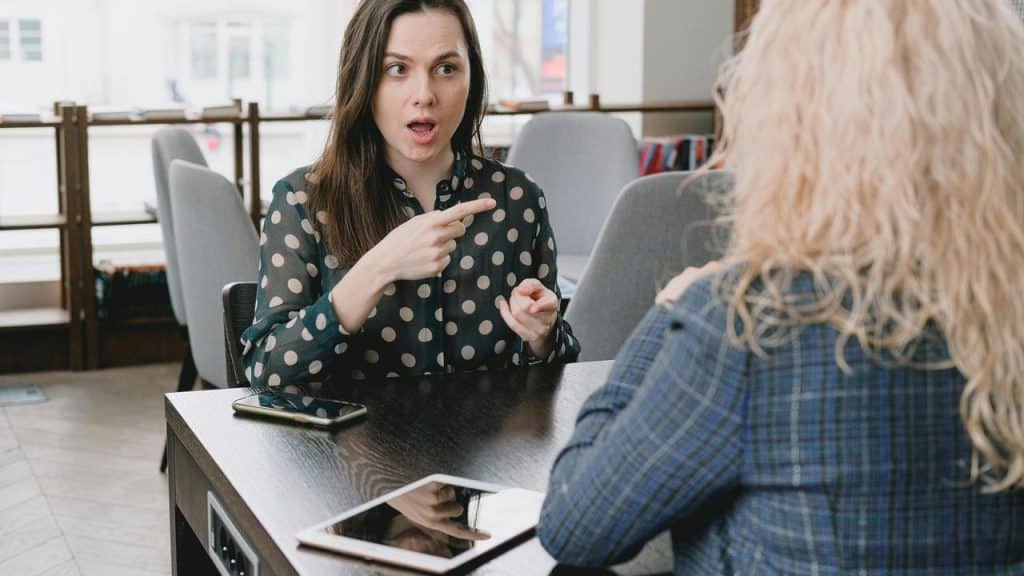 A woman gesturing while talking to another person at a table.