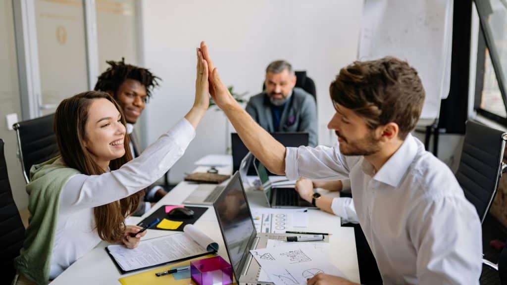 A woman and man give each other a high five across a desk in an office.