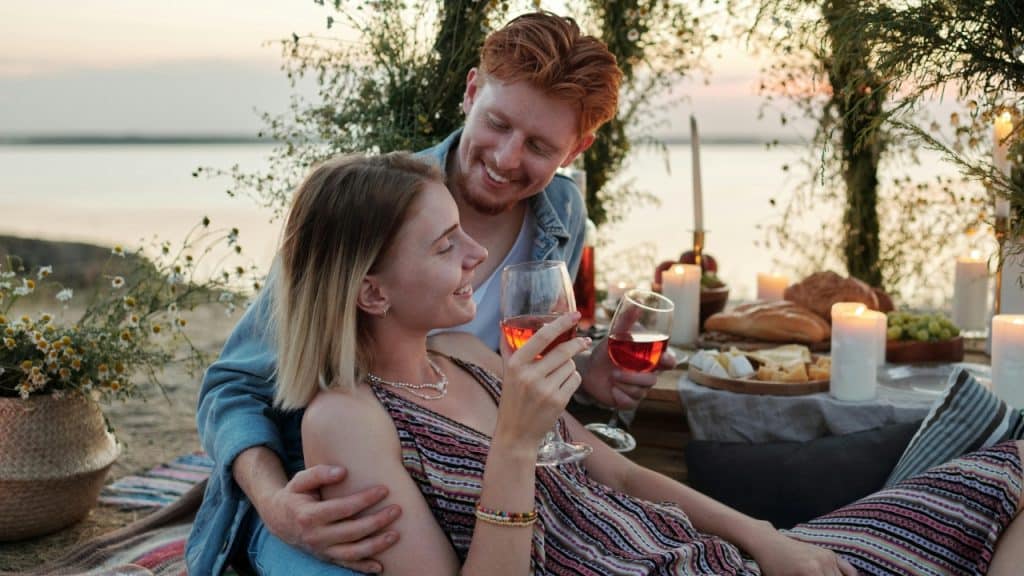 A couple holding wine glasses while sitting together at a romantic outdoor picnic.