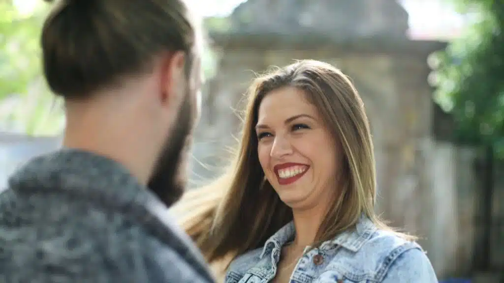 A woman with long hair smiles while looking at a man whose back is turned.