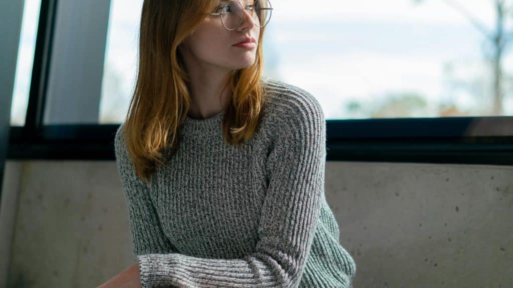 A woman wearing glasses and a gray sweater looks to the side