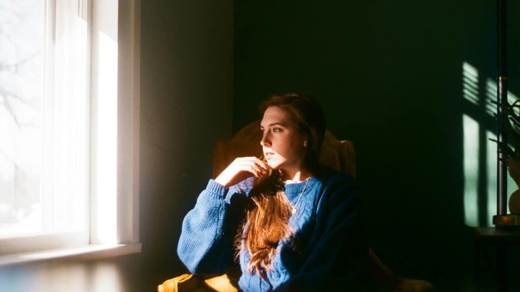 A woman sitting by a window looking thoughtful.
