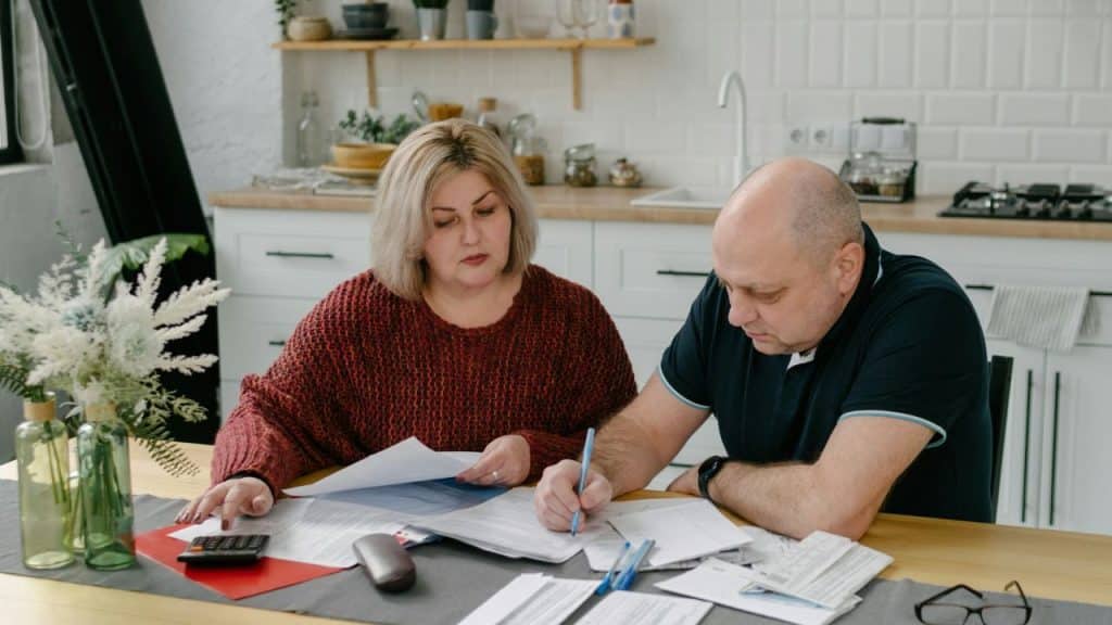 A woman and man sit at a table reviewing paperwork with a calculator and pen.