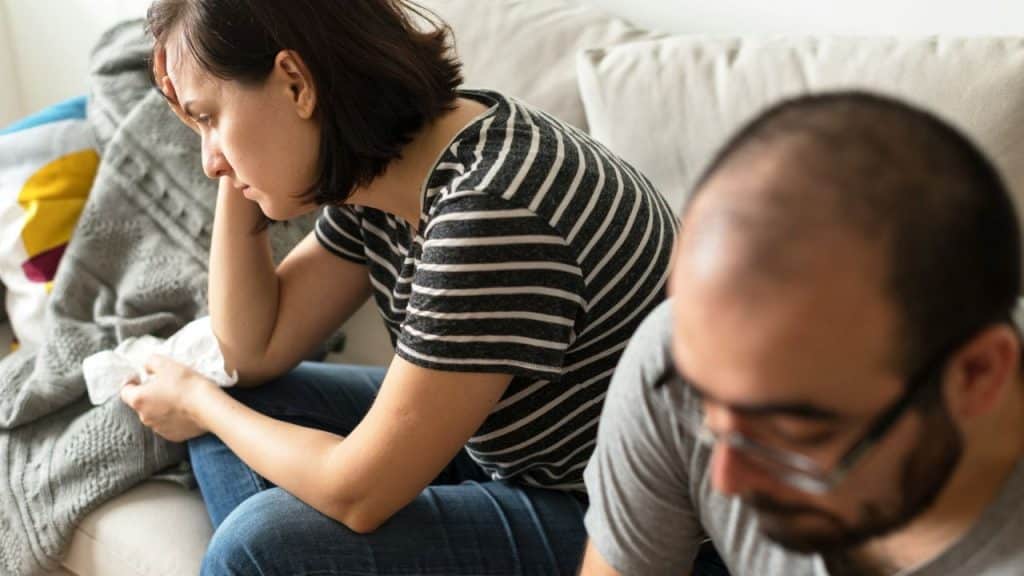 A woman looks down sadly while a man in the foreground looks away from her.