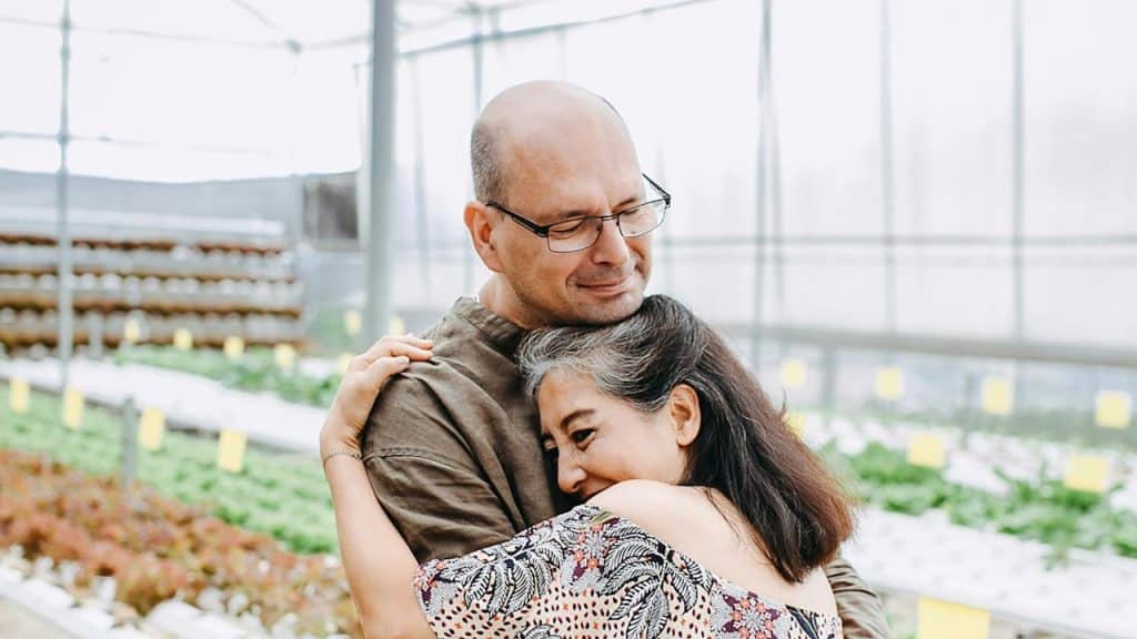 A mature couple hugging in a greenhouse.