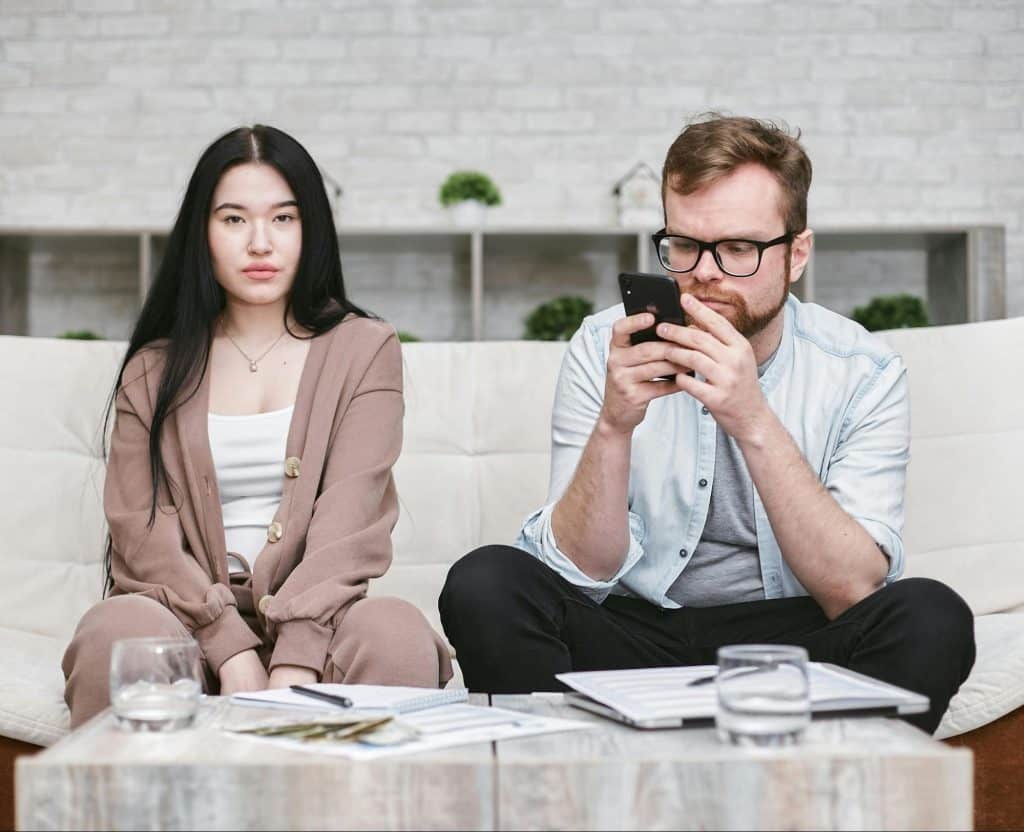 Woman staring and a man busy with phone