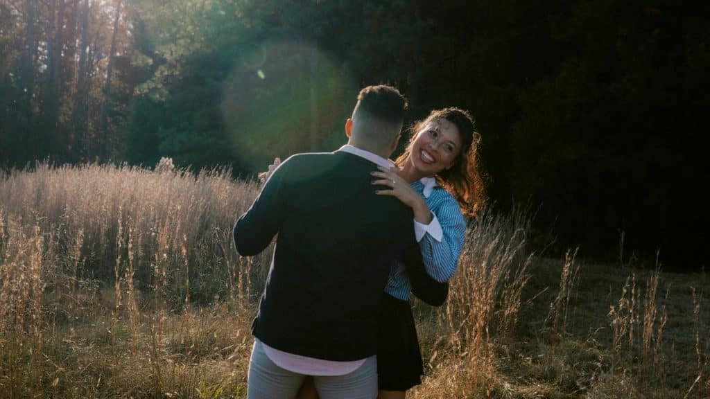 A couple dancing together in a sunlit field surrounded by tall grass.
