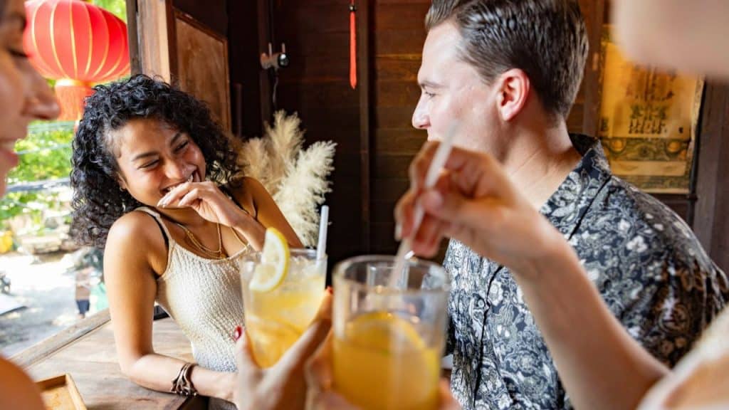 A woman laughs while sitting at a bar with friends holding drinks with lemon slices.