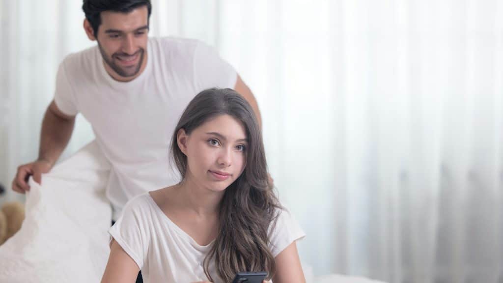 A man looking at his wife using a phone while standing behind her.