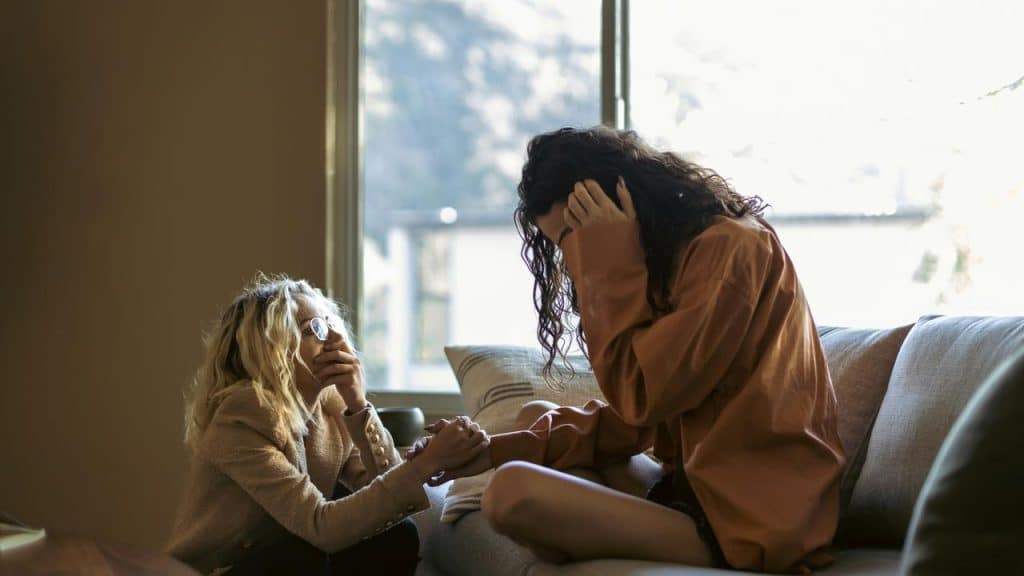 A woman comforting another woman who appears distressed while sitting on a couch.