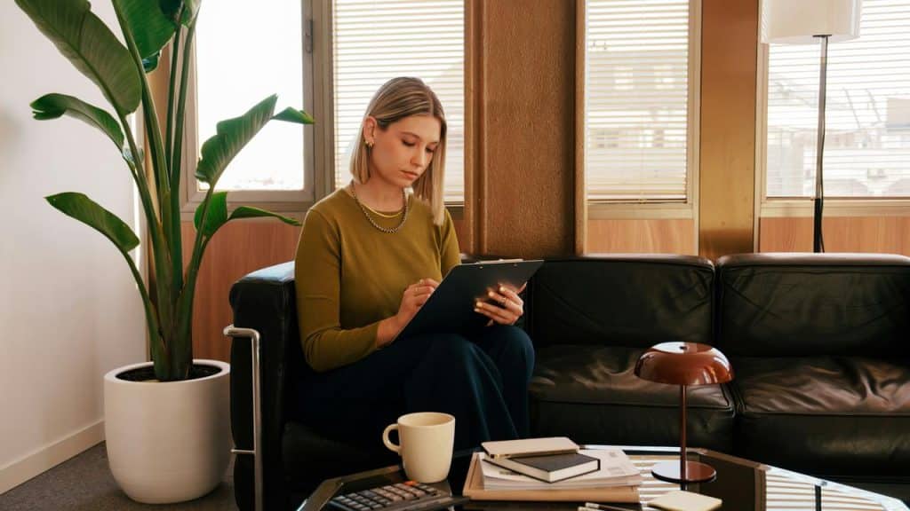 A woman sitting on a couch writing on a clipboard in a cozy living room.
