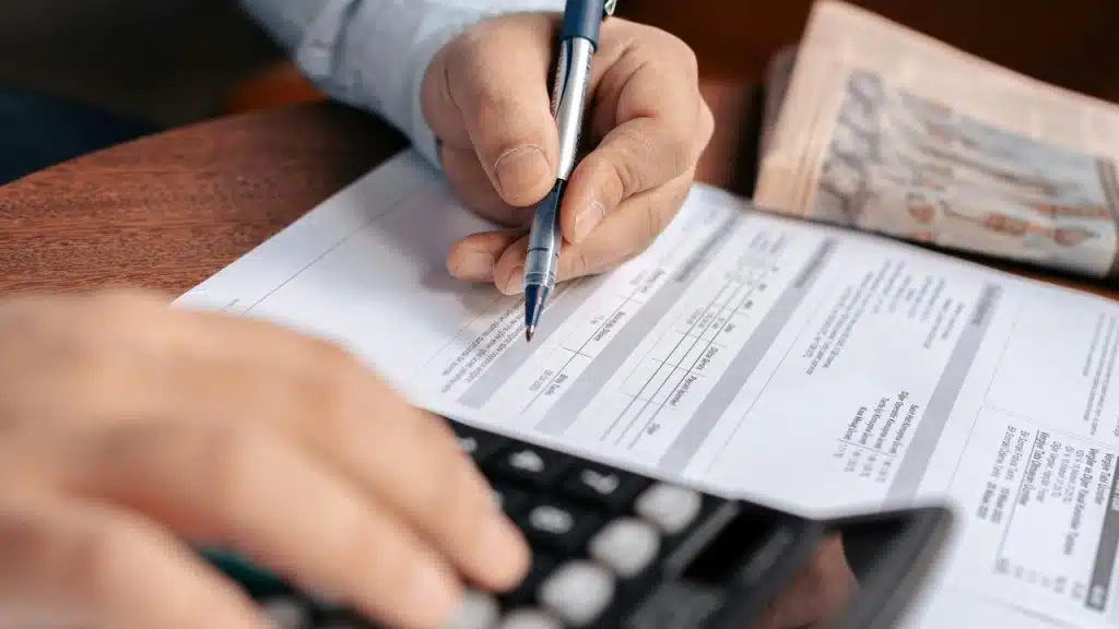 A person using a calculator while reviewing and marking a financial document.
