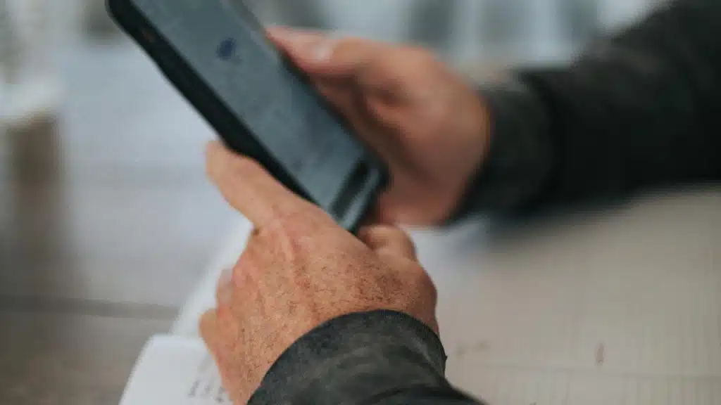 A person holds a smartphone while reading or typing at a desk.