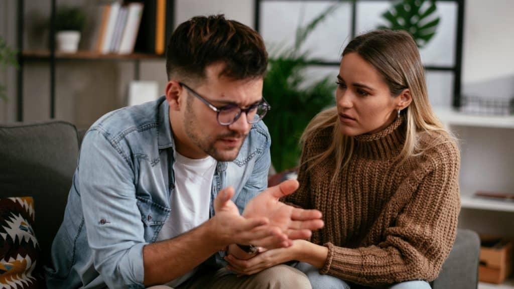 A woman in a brown sweater looking at a man in a denim shirt gesturing.