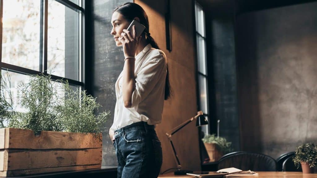 A woman standing by a window talking on her phone.