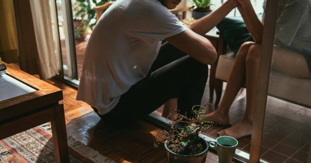 A person crouching indoors while holding hands with someone seated nearby.