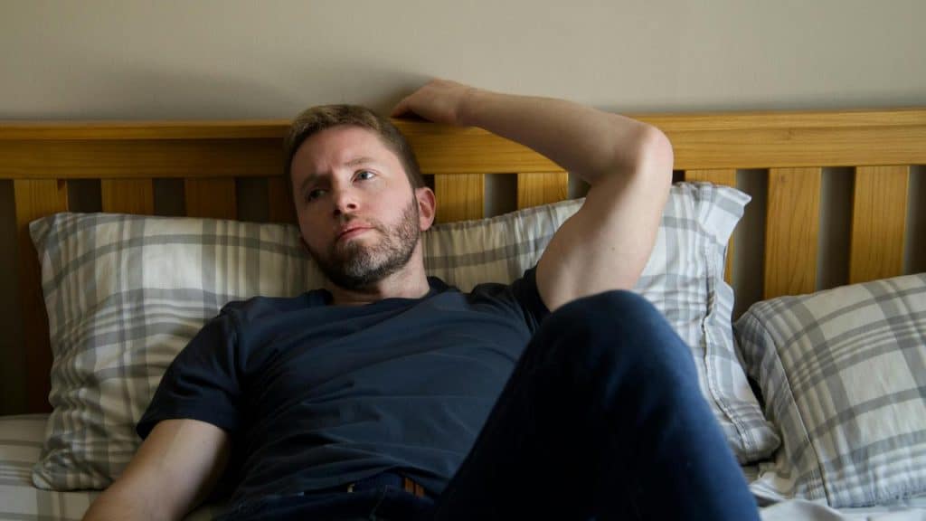 A man lying on a bed and staring thoughtfully at the ceiling.