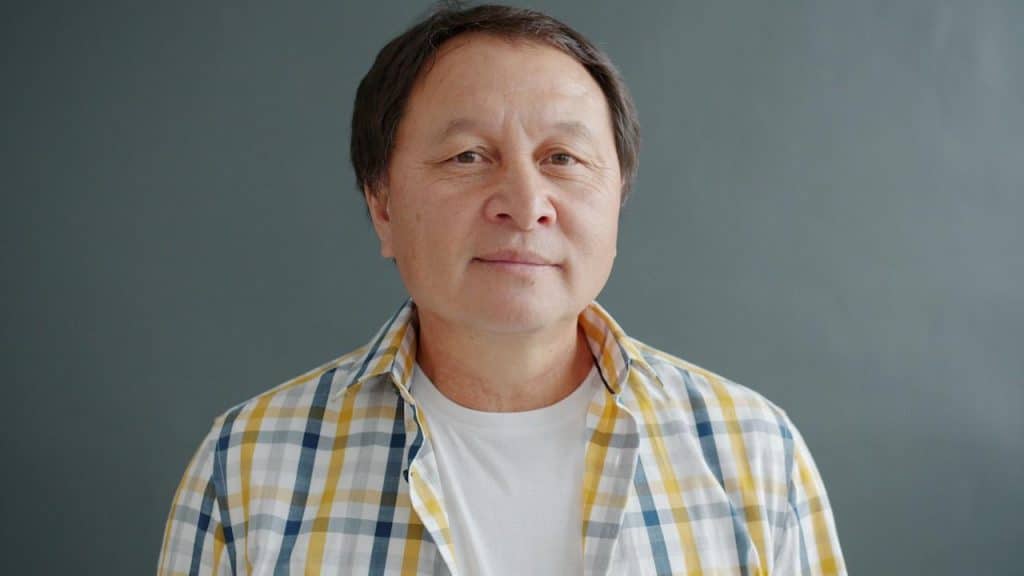 An older Asian man wearing a plaid shirt.