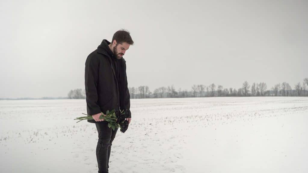 A man standing in the snow holding a bouquet of flowers.