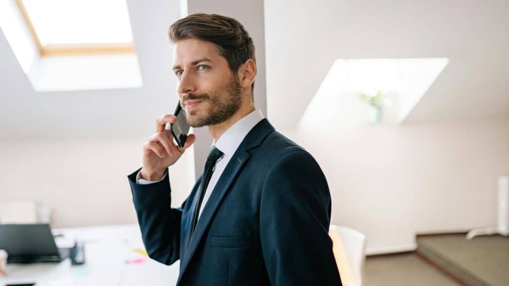 A man in a suit talking on a smartphone in a bright office.