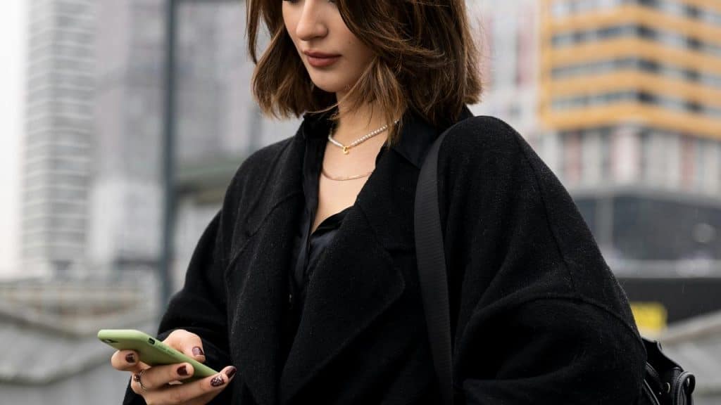A woman standing outdoors and looking down at her smartphone.