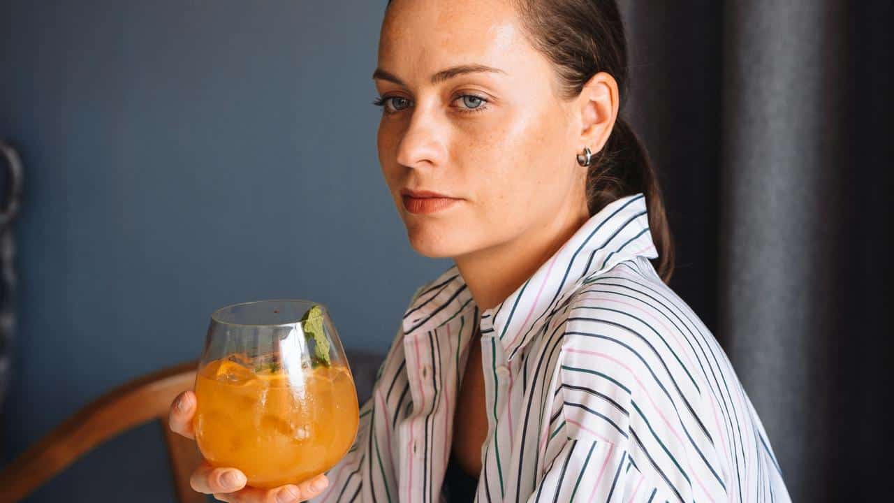 A woman holding an orange drink and looking thoughtfully to the side.
