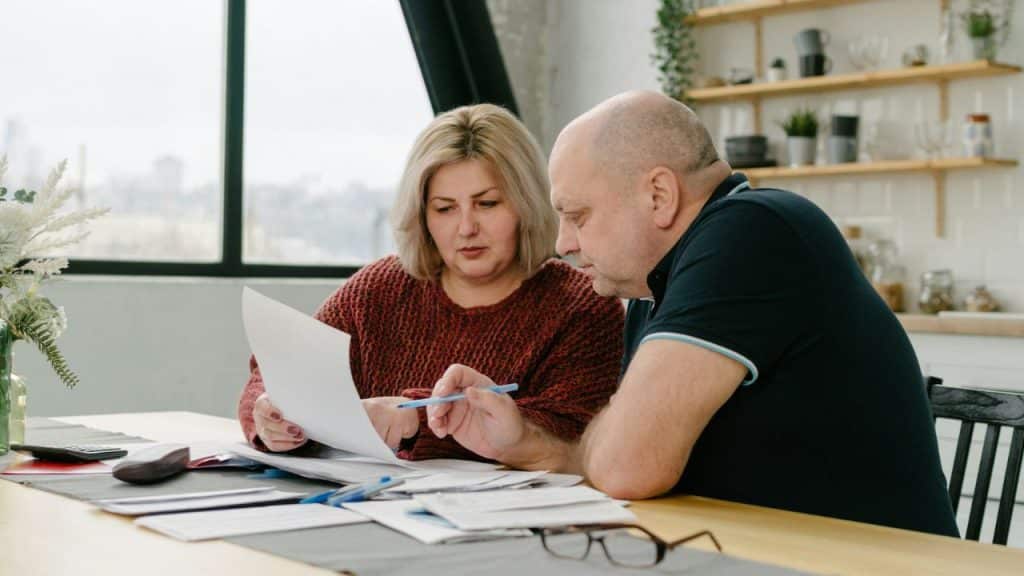 A man and woman sit at a wooden table together reviewing a white paper document.